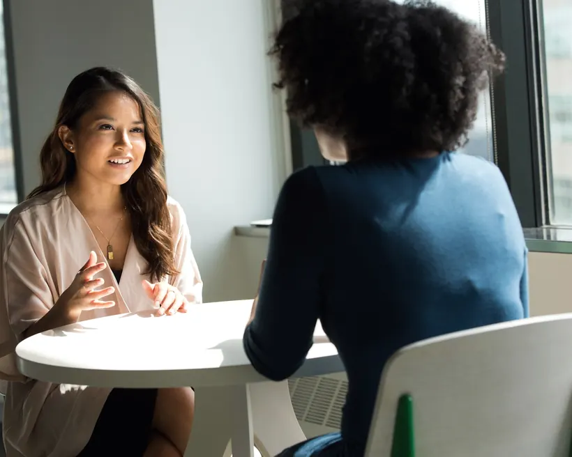 Two women talking calmly across a small table beside a bright window